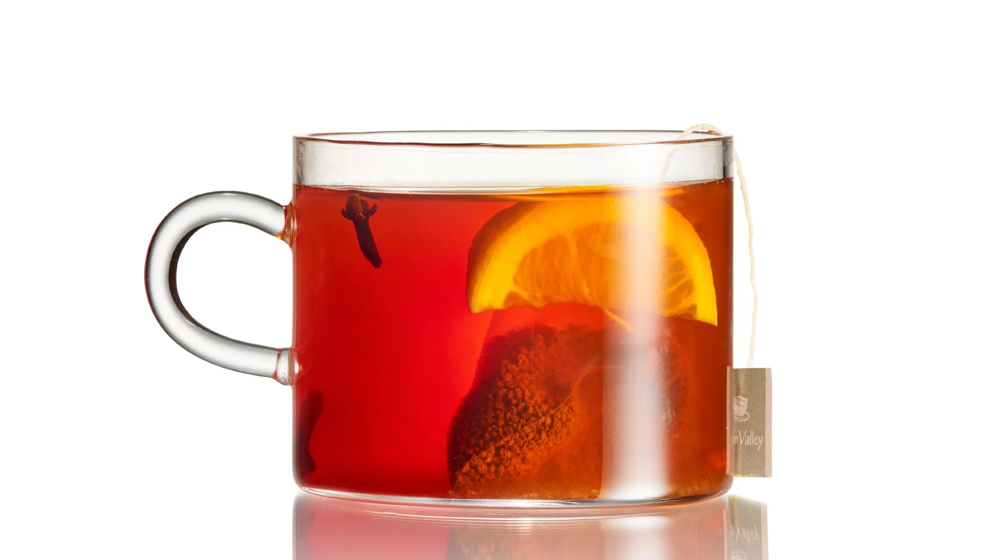 a squat glass mug filled with dark-orange liquid. there is a tea bag, clove and orange wedge floating in the liquid