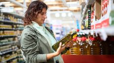 Woman in a grocery comparing prices of different olive oil bottles